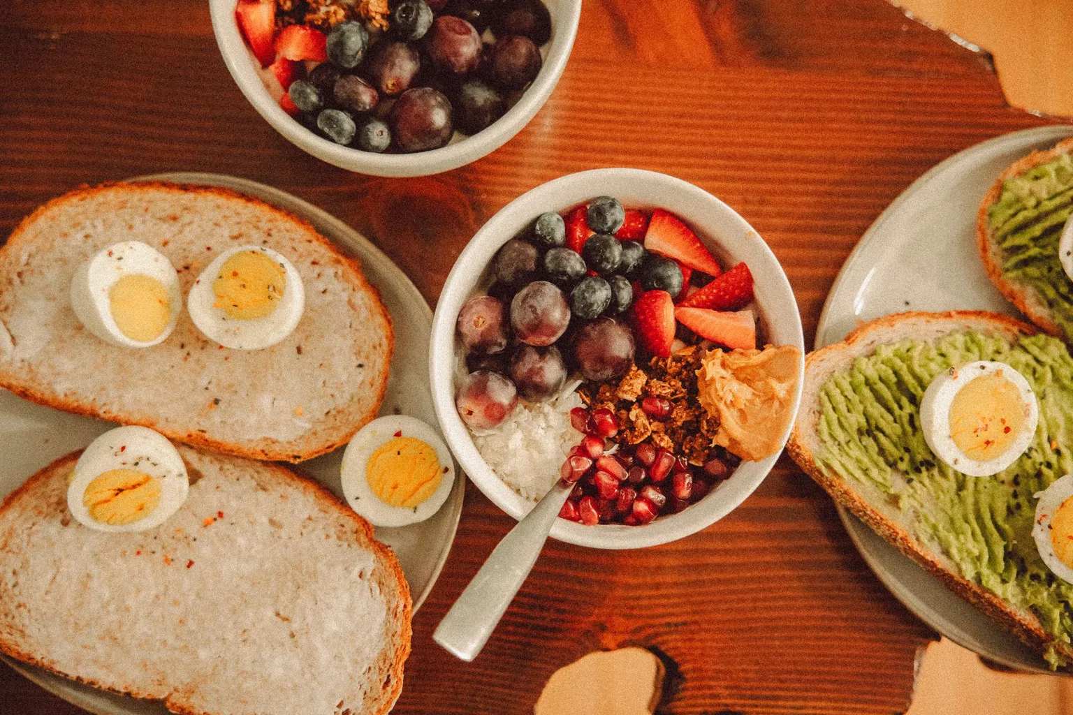 Overhead view of a breakfast table with eggs on toast and a bowl of yogurt with fruit