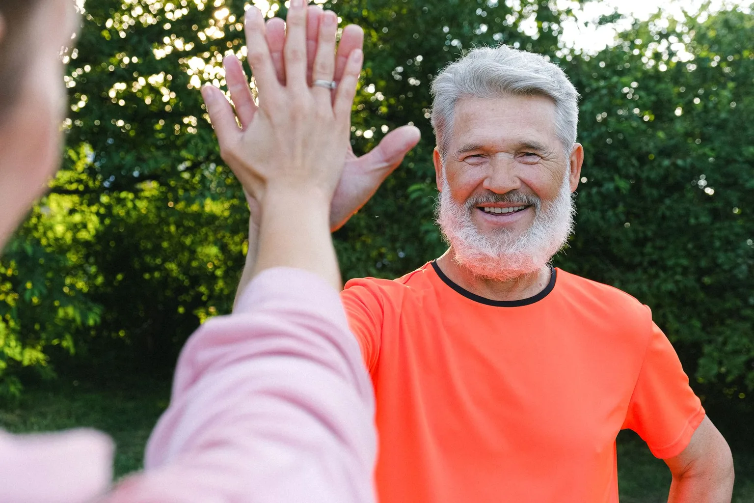 Smiling silver-bearded man in training clothes giving a high five outdoors after a workout